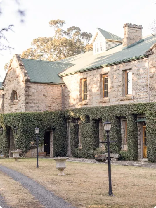 Ivy-covered stone manor house with lamp posts along a gravel drive